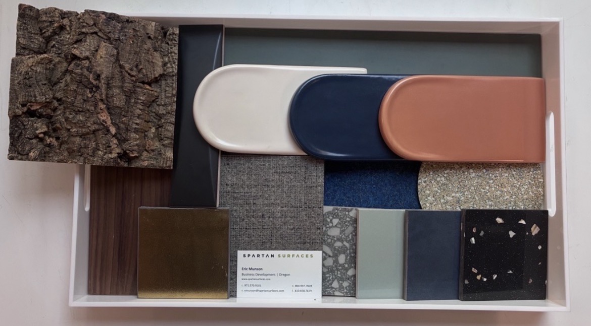 Display tray of architectural surface samples — cork, wood, metal, ceramic, textile and terrazzo — with a Spartan Surfaces business card